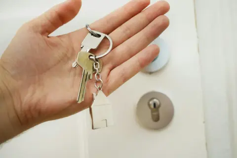 En hand håller nycklar med ett hus som berlock. Dags att byta lås och få nya nycklar till hemmet.