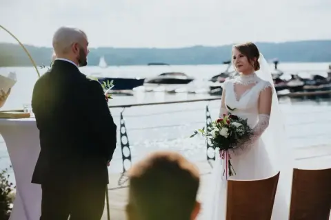 Para młoda podczas ślubu rzymskiego nad jeziorem. Panna młoda w białej sukni z bukietem, pan młody w garniturze.