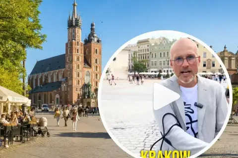 Mężczyzna w okularach opowiada o tym, czy jest krakow safe, na tle Rynku Głównego z Kościołem Mariackim.