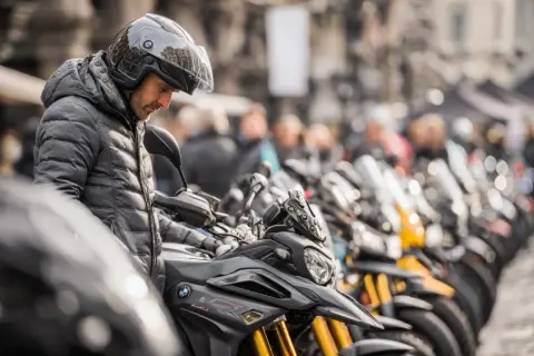 Mężczyzna w kasku ogląda lekki motocykl. W tle rząd innych motocykli i ludzi.