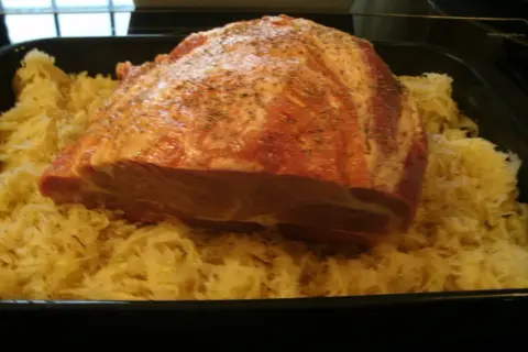 Rohes Schweinefleisch mit Gewürzen liegt auf Sauerkraut in einer Bratreine. Bereit zum Kochen.