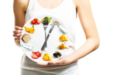 Une assiette en forme d'horloge illustrant la chrono nutrition avec des fruits, légumes, pain et eau.