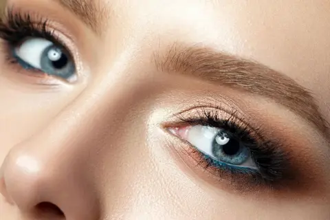 Blonde Haarfarbe betont blaue Augen. Nahaufnahme eines weiblichen Auges mit blauem Eyeliner und goldenem Lidschatten.