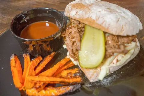 Pulled pork-macka med krispiga sötpotatispommes och en skål med smakrik sås till pulled pork.
