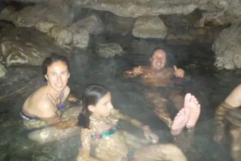 Familia disfrutando de las pozas termales del río Deva, rodeados de rocas y agua cálida.