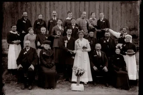 Un groupe de familles posant pour un recensement ad 88. La mariée, en blanc, tient un bouquet.