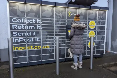 Paczkopunkt InPost: odbierz, zwróć, wyślij paczkę. Kobieta korzysta z automatu.