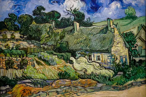 Ein Dorf mit strohgedeckten Häusern und üppiger Vegetation, typisch für die Werke van Goghs. Der Himmel ist dramatisch blau mit wirbelnden Wolken.