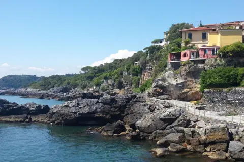 Case colorate su una scogliera rocciosa, con il mare blu e il cielo limpido. Un sentiero panoramico si snoda lungo la costa, ricordando la bellezza della riviera delle palme San Benedetto del Tronto.