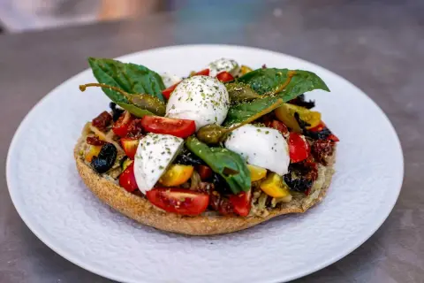 Frisches Brot belegt mit Tomaten, Kapern, Oliven und verschiedenen Mozzarella Arten, garniert mit Basilikum.