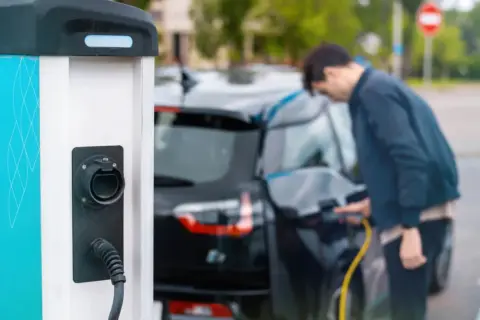 Mężczyzna ładuje czarny samochód elektryczny przy stacji ładowania.