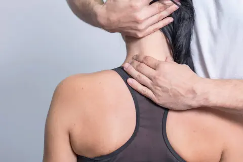Hände massieren den verspannten Nacken einer Frau.