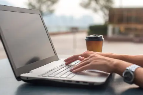 Kobieta pisze na laptopie, zastanawiając się, co zainstalować na nowym komputerze. Obok stoi kubek kawy.
