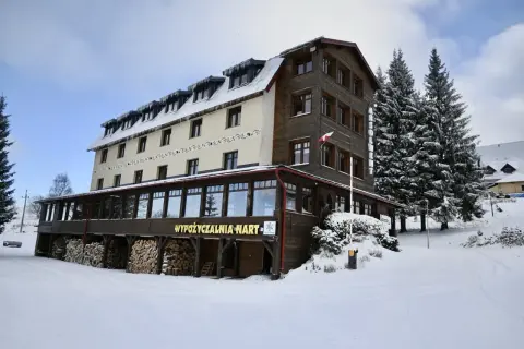 Zimowy hotel z drewnianymi elementami, idealny na zieleniec noclegi blisko stoku. Wokół śnieg i wysokie choinki.