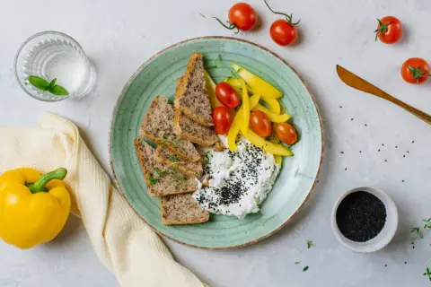 Szybkie posiłki wysokobiałkowe: twarożek z czarnuszką, pieczywo, pomidorki i papryka. Idealne na lekki lunch.