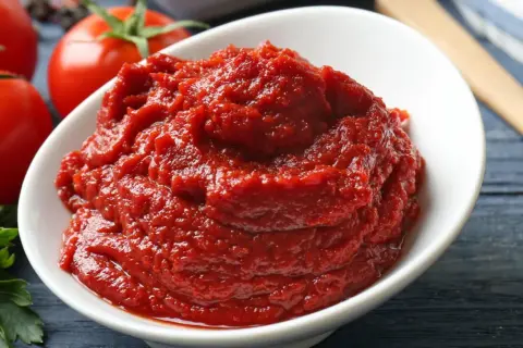 Schüssel mit selbstgemachtem Tomatenmark, daneben frische Tomaten.