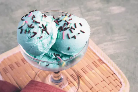 Zwei Kugeln blaues Eis mit bunten Streuseln in einem Glas auf einem Holzuntersetzer.