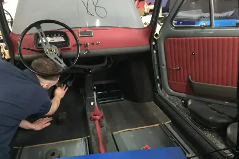 Der Mann arbeitet am fiat 500 oldtimer innenraum. Rote Türverkleidung und Armaturenbrett sind sichtbar.
