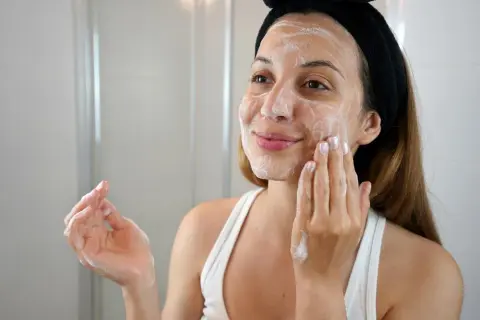Mujer con espuma en el rostro, aplicándose un limpiador facial con ácido glicólico y niacinamida.