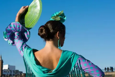 Bailarina de flamenco con abanico verde, evocando el flamenco origine. Su vestido vibrante y flor en el pelo resaltan la pasión.