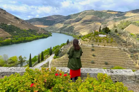 Mujer admira la impresionante **ruta del Duero**, con sus viñedos en terrazas y el río serpenteando entre colinas verdes.