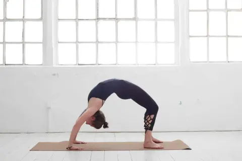Frau in schwarzer Kleidung in einer Brückenpose, eine der yoga posen schwer, die Kraft und Flexibilität zeigt.