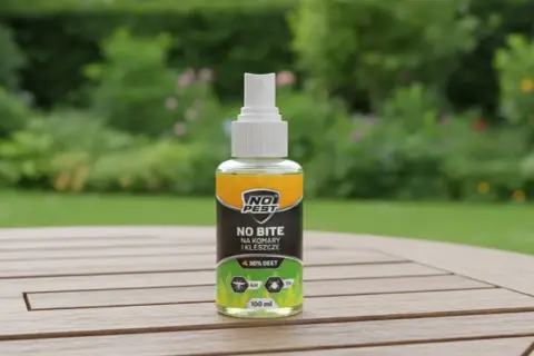 Butelka sprayu "No Bite" z 30% DEET, najmocniejszy środek na komary i kleszcze, na drewnianym stole w ogrodzie.