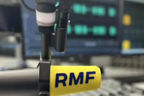 Mikrofon radiowy z logo RMF FM na tle ekranu z falami dźwiękowymi.