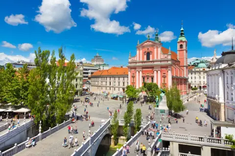 Tętniący życiem plac w Lublanie, stolicy Słowenii, z różową katedrą i mostami pełnymi ludzi.