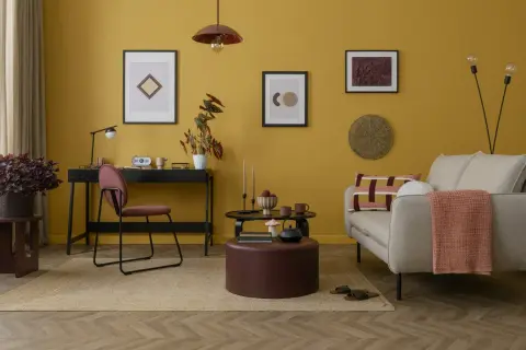 Un accogliente soggiorno con pareti color ocra, un divano beige, una scrivania nera e un tavolino rotondo.