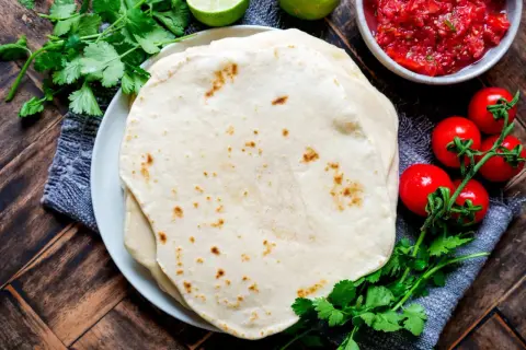 Frische Tortillas, perfekt für jedes Tortilla Rezept, mit Salsa, Tomaten und Koriander auf Holztisch.