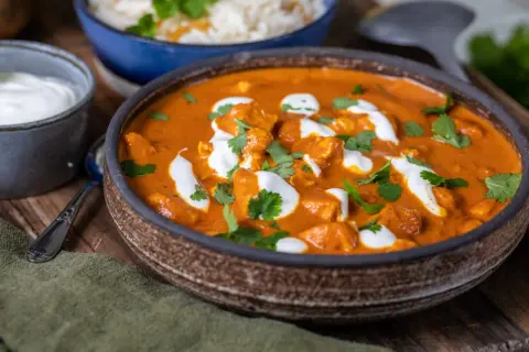 En krämig tikka masala med kycklingbitar, toppad med grädde och koriander. Serveras med ris och en skål yoghurt.