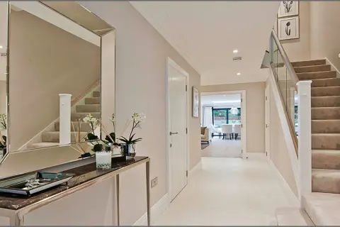 Ingresso moderno con specchio, consolle, scale e porta aperta su un'altra stanza.