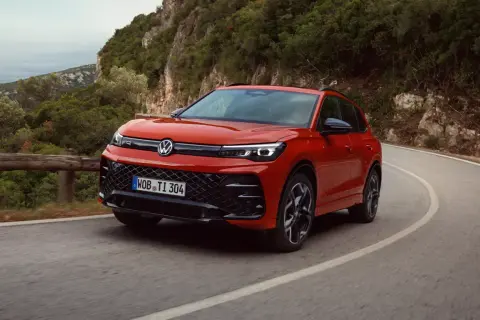 Röd Volkswagen kör på en kurvig väg i bergen. Denna hybridbil kombinerar eldrift med bensinmotor, vilket ger en flexibel körupplevelse.
