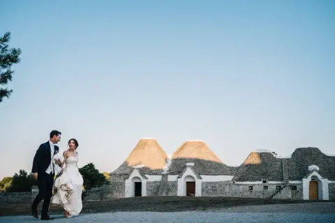 Sposi passeggiano sorridenti davanti a trulli, un'immagine perfetta per le canzoni ingresso sposi.