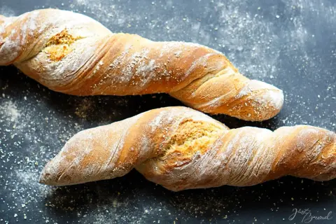 Zwei gedrehte Brote, die an ein Wurzelbrot Rezept dunkel erinnern, liegen auf dunklem Untergrund, bestäubt mit Mehl.