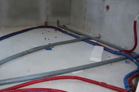 Na betonowej posadzce widać instalację wodną z czerwonych i niebieskich rur, które tworzą skomplikowany trojnik.