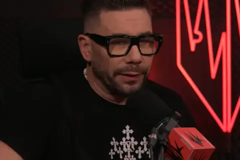 Mężczyzna w okularach i czarnej koszulce z krzyżami, kto prowadzi szalony podcast.