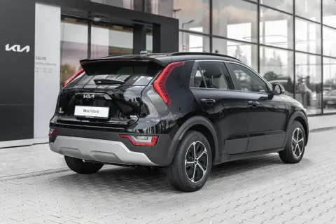 Czarny Kia Niro Hybrid stoi przed salonem. Elegancki tył auta z charakterystycznymi światłami i napisem "Niro Hybrid" przyciąga wzrok.