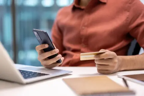 Mężczyzna trzyma telefon i kartę, szukając informacji, jak anulować subskrypcję.