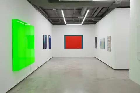 Galeria sztuki z neonowo-zieloną instalacją i obrazami, w tym dziełem Stefana Gierowskiego.