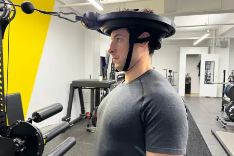 Man performing neck curls with a weighted harness in a gym.