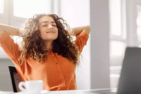 Femme souriante, mains derrière la tête, profitant d'une pause. Son retour congé maternité obligation employeur semble bien se passer.