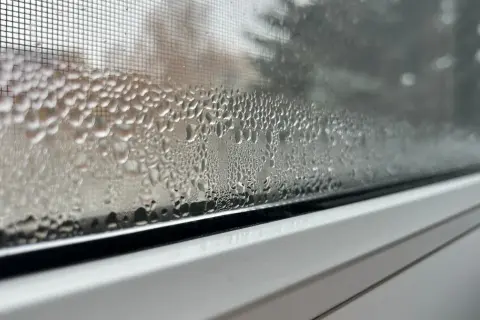 Krople wody na siatce moskitiery w oknie plastikowym tworzą ciekawy wzór, jakby małe perełki.