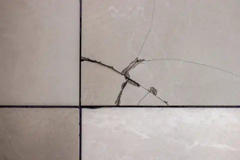 Gros plan sur un carrelage beige fissuré, montrant les étapes pour comment reparer un eclat de carrelage.