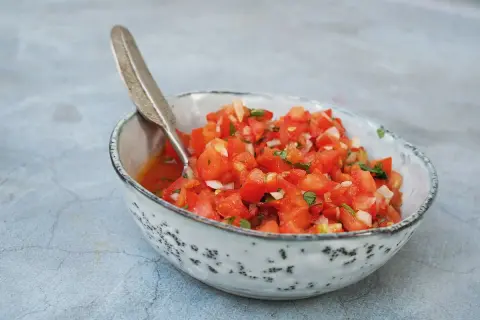 En skål med färsk pico de gallo, perfekt för ditt salsa recept. Tomater, lök och örter blandas i en rustik skål med en dekorativ sked.