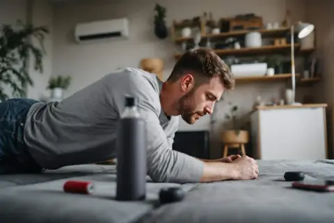 Un homme en position de planche, réfléchissant à comment faire du sport quand on a pas le temps. Une bouteille d'eau et un téléphone sont à proximité.