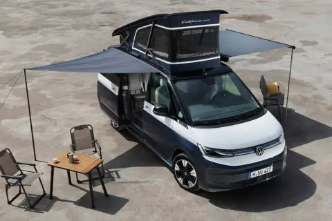 La vw california electrica lista para la aventura, con toldo extendido, mesa y sillas, lista para disfrutar del aire libre.