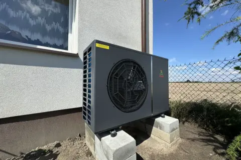 Nowoczesna pompa ciepła Geo Power, która obniża koszt ogrzewania domu. Urządzenie stoi na betonowych bloczkach przy ścianie budynku.
