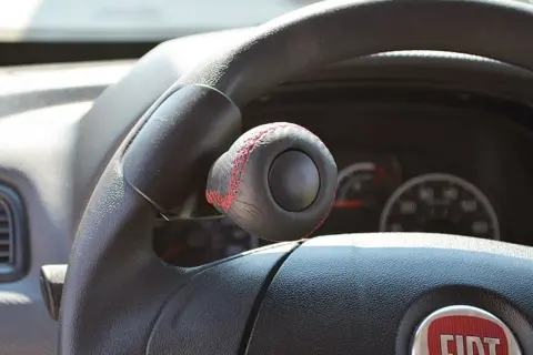 Pomello volante in pelle nera con cuciture rosse, un accessorio che rispetta la normativa per una guida sicura e personalizzata.